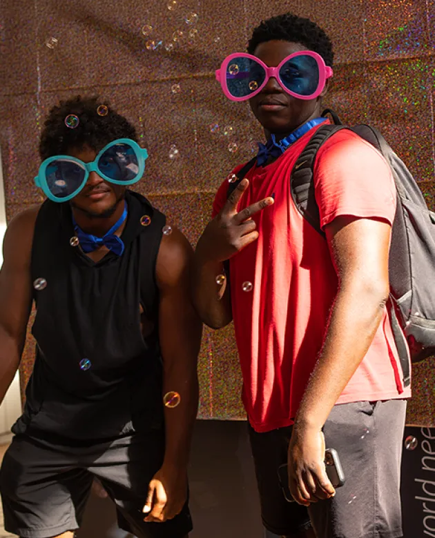Two students in a photobooth pose in front of a glittery background