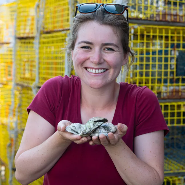 a students holds two handfuls of clams in front of fishing traps