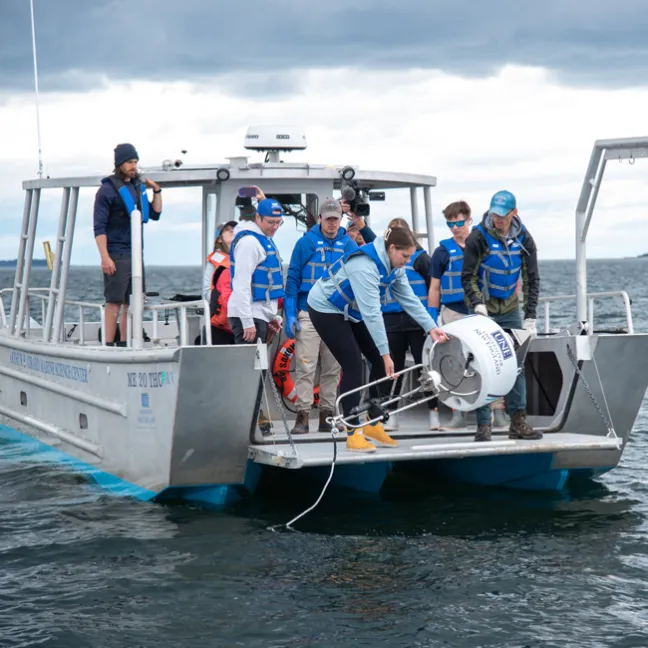 A group of students on a U N E boat retreive a white shark buoy from the ocean