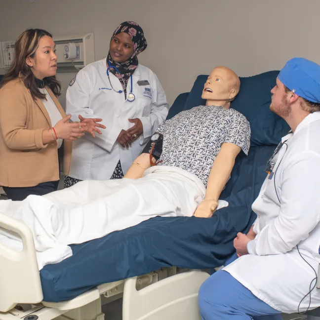 A group of students from different health programs discuss a diagnosis over a patient simulator