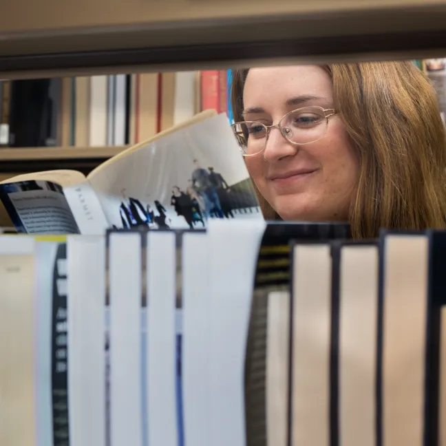 A student reading a book in the Ketchum Library library stacks