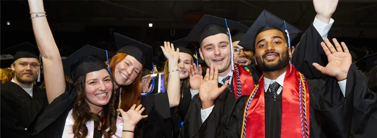 U N E graduates in caps and gowns wave during commencement.