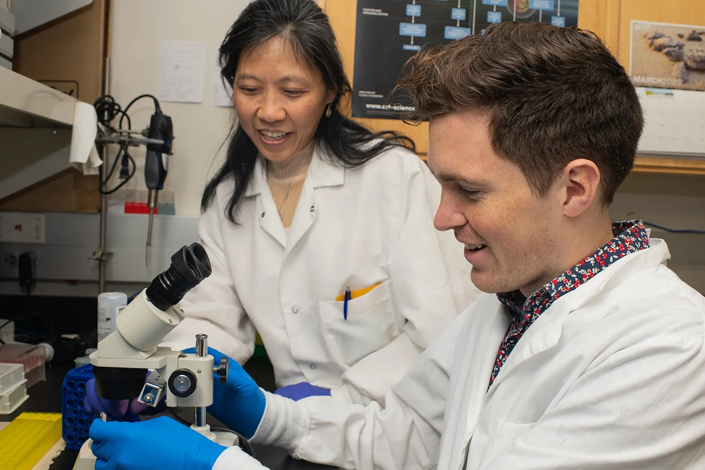 A research professor helps a student with a microscope