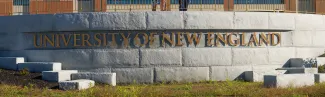 A metal sign against a brick wall reads "University of New England"