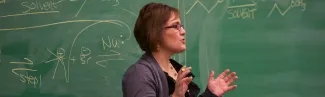 A faculty member stands in front of a chalkboard