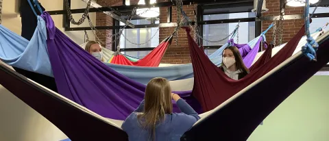 Two female students sit in a hanging tool for children at an occupational therapy clinic