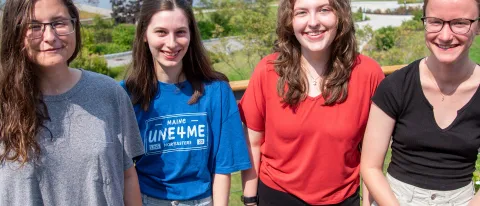 Four students who have received the Millennium Fellowship pose on a campus deck. The campus quad is visible at back