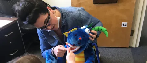 Dental student Ayla Nelson helps a young patient practice her toothbrushing skills using a stuffed animal