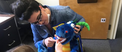 Dental student Ayla Nelson helps a young patient practice her toothbrushing skills using a stuffed animal