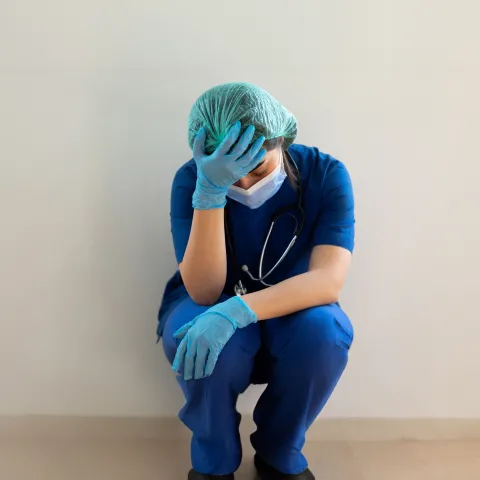 An image of a health worker in scrubs holding their head in disbelief 